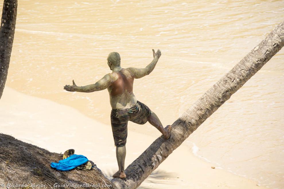Imagem de um rapaz cheio de lama sob caule do coqueiro.